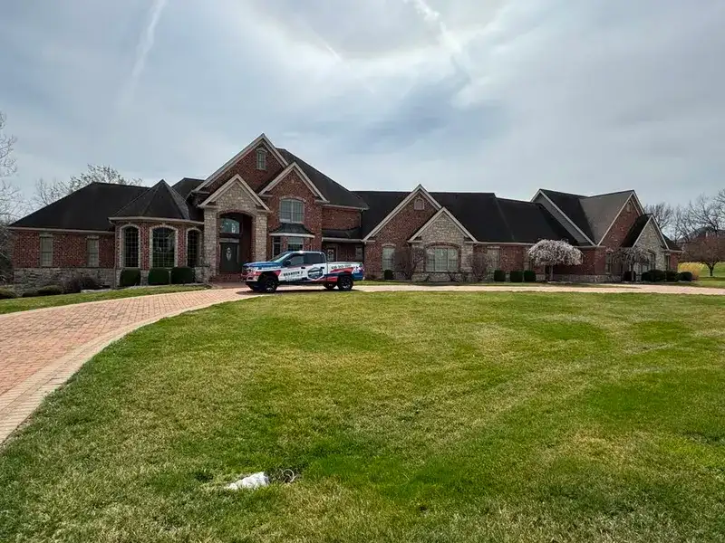 Completed roof replacement on a large brick home with the company truck in the driveway