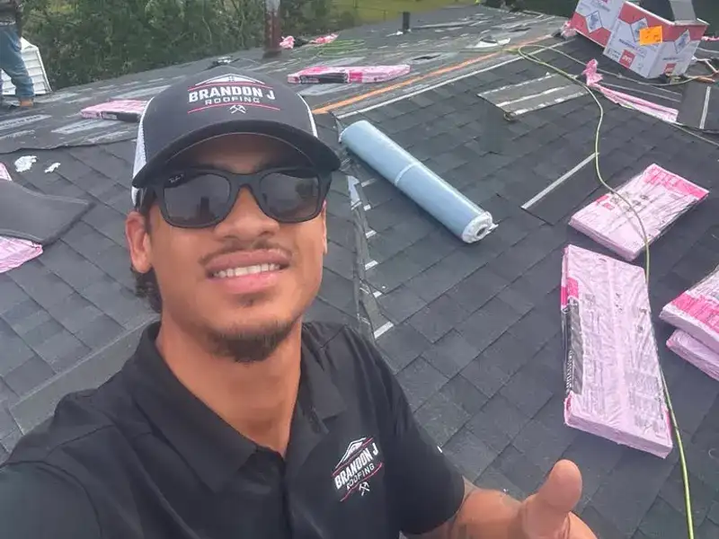 Nate Desemone on a residential roof during a Brandon J Roofing replacement, wearing branded cap and polo