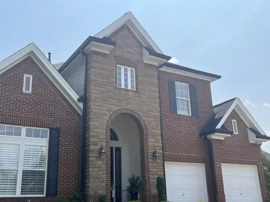 New seamless gutters and downspouts installed along the eaves of a brick home